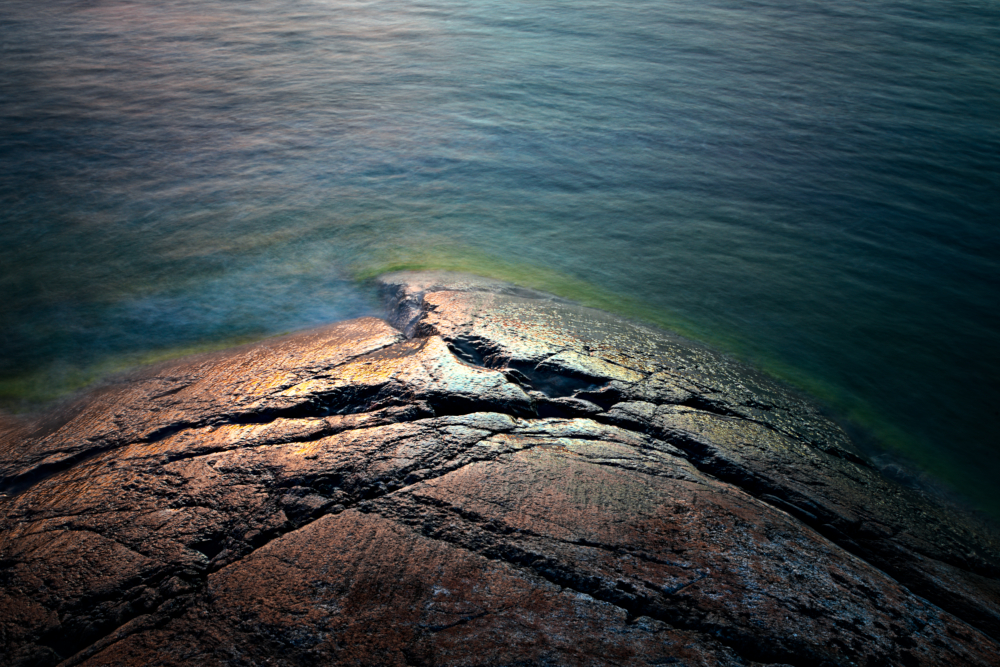 Solens spegling på klippor i Ålands skärgård. Lång exponeringstid med suddiga vågor.